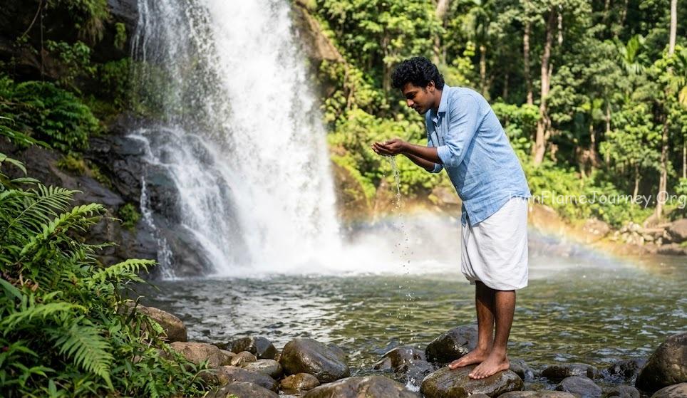 A young South Indian man from Kerala cups natural waterfall water in his hands, connecting with the energy of nature.