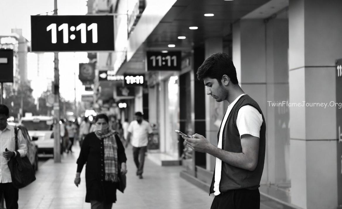 A bustling street scene in a modern setting. A young Pakistani man (age 19) is looking at his phone showing 11:11