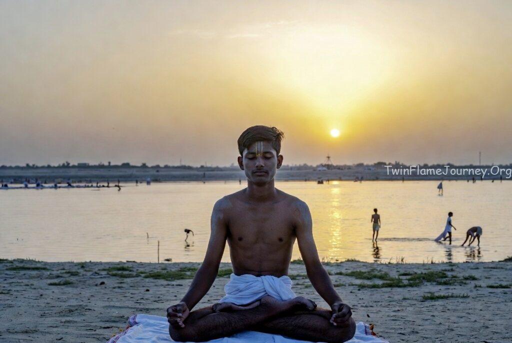 DM with a calm expression, sitting in a meditative pose near the Ganges river at sunset